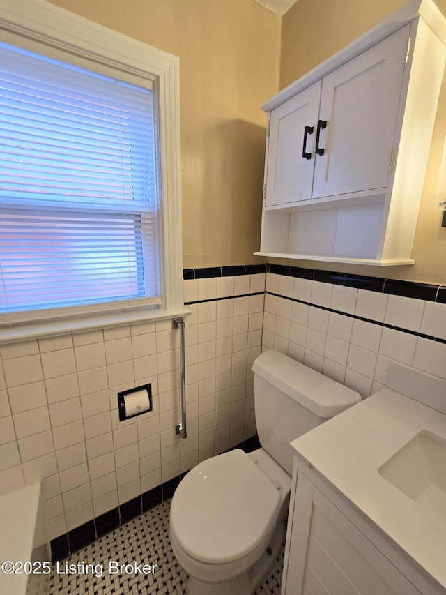 bathroom featuring wainscoting, a sink, toilet, and tile walls