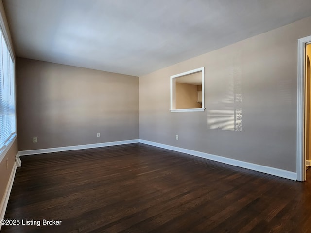 spare room featuring dark wood-style floors and baseboards