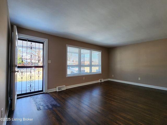 unfurnished room featuring baseboards, visible vents, and dark wood-type flooring