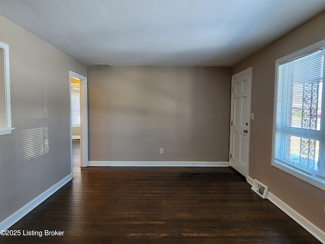 empty room featuring baseboards, visible vents, and dark wood-style flooring