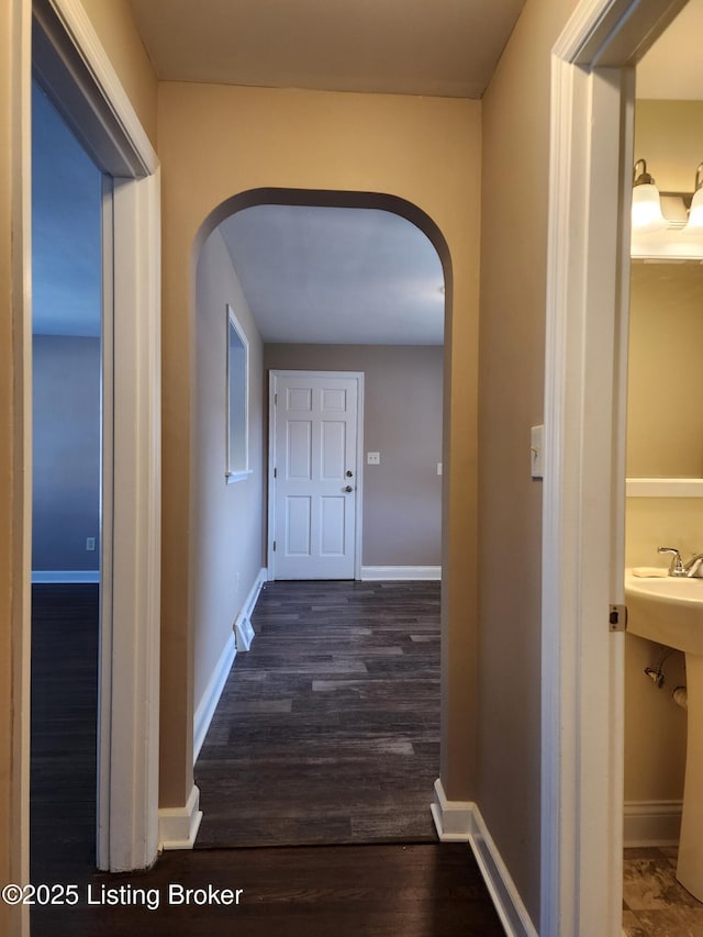 corridor with dark wood-style floors, arched walkways, and baseboards