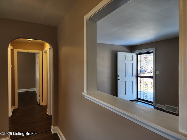 hall featuring baseboards, visible vents, arched walkways, and dark wood-type flooring