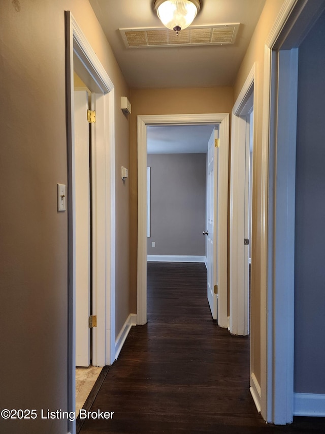 corridor featuring visible vents, baseboards, and wood finished floors