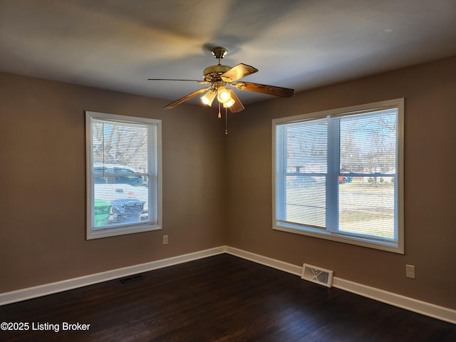 unfurnished room with a wealth of natural light, visible vents, dark wood finished floors, and baseboards