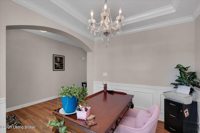 office area with arched walkways, wood finished floors, a wainscoted wall, and a raised ceiling