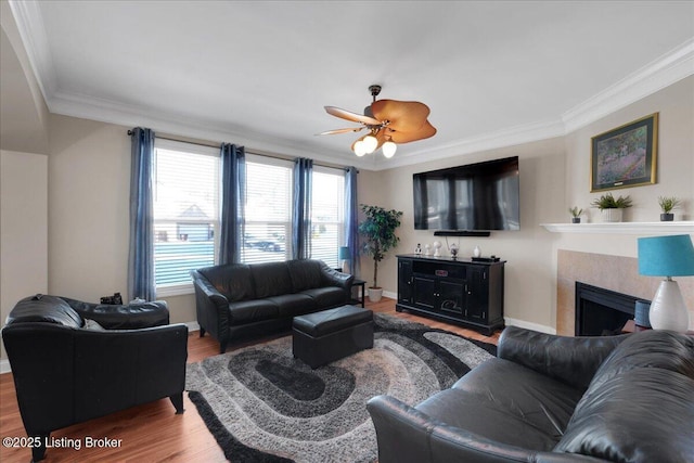 living room featuring a fireplace, ornamental molding, a ceiling fan, wood finished floors, and baseboards