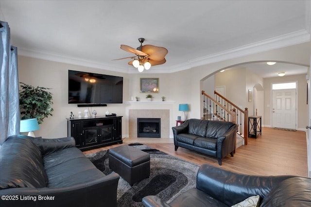 living area with light wood-style floors, stairs, arched walkways, and crown molding