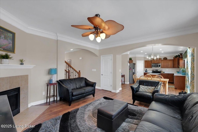 living area with arched walkways, baseboards, ornamental molding, light wood finished floors, and a tiled fireplace