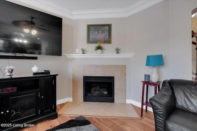 living area featuring ornamental molding, a tiled fireplace, wood finished floors, and a ceiling fan