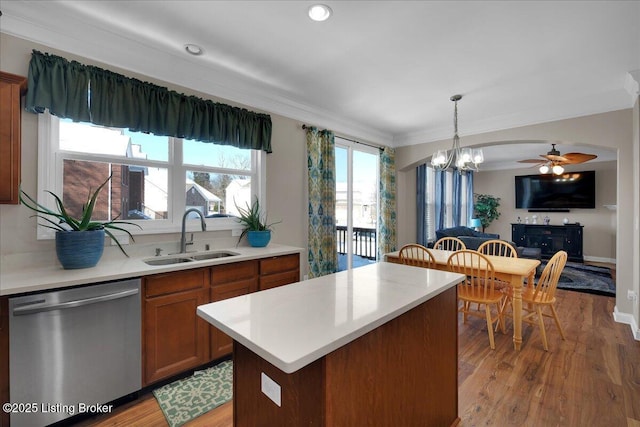 kitchen with a sink, light countertops, stainless steel dishwasher, brown cabinets, and decorative light fixtures