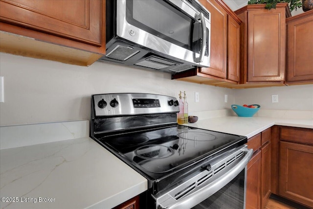 kitchen featuring stainless steel appliances, brown cabinetry, and light countertops