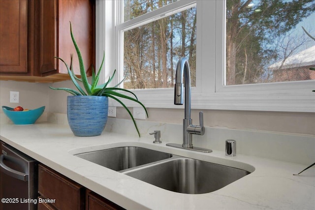 interior details featuring light stone counters, a sink, and dishwasher