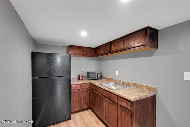 kitchen with light wood-style flooring, a sink, light countertops, freestanding refrigerator, and stainless steel microwave