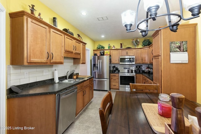 kitchen featuring decorative backsplash, dark countertops, appliances with stainless steel finishes, brown cabinets, and a sink