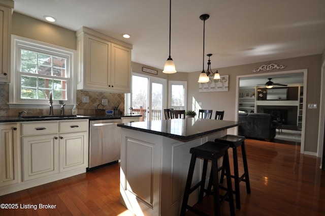 kitchen with dark wood-style flooring, a fireplace, dark countertops, stainless steel dishwasher, and a sink