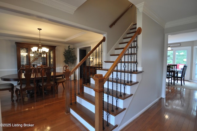 staircase with wood-type flooring, a notable chandelier, crown molding, and baseboards