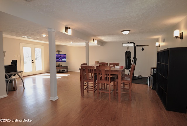 dining space featuring french doors, ornate columns, a textured ceiling, wood finished floors, and baseboards