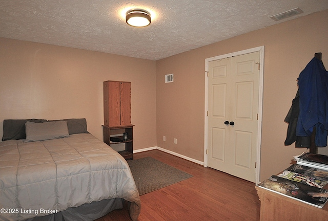 bedroom with visible vents, a textured ceiling, baseboards, and wood finished floors