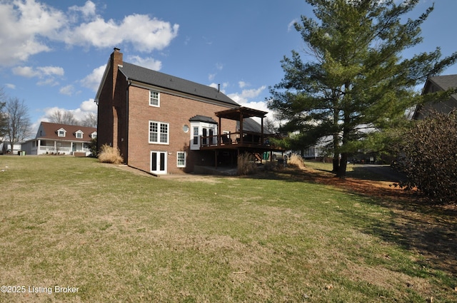 rear view of house with brick siding, a yard, a chimney, and a wooden deck