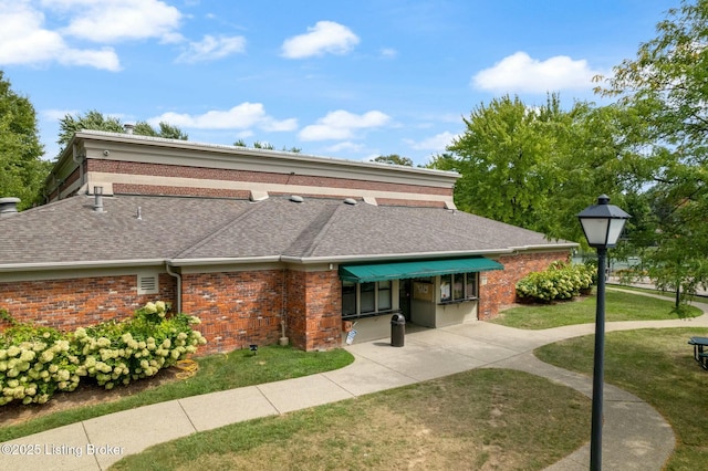 view of front of home featuring a front lawn, a shingled roof, and brick siding