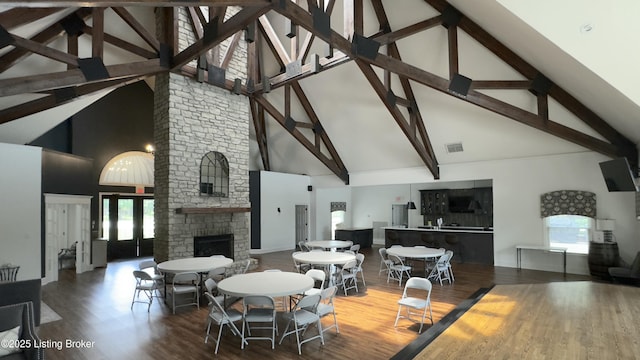 dining space featuring plenty of natural light, beam ceiling, wood finished floors, and a stone fireplace