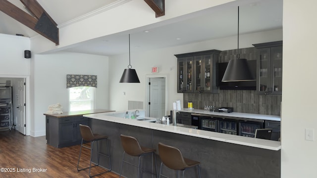 kitchen with decorative backsplash, dark wood-type flooring, glass insert cabinets, wall chimney range hood, and a kitchen bar