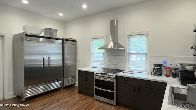 kitchen featuring tasteful backsplash, dark wood finished floors, wall chimney exhaust hood, appliances with stainless steel finishes, and dark cabinets