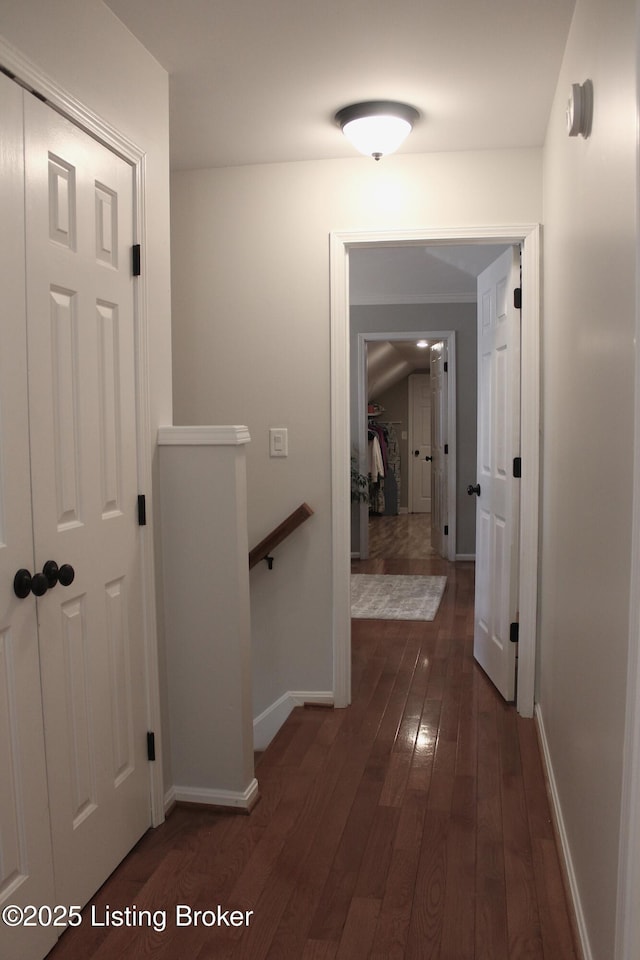 hallway with dark wood-type flooring, an upstairs landing, and baseboards