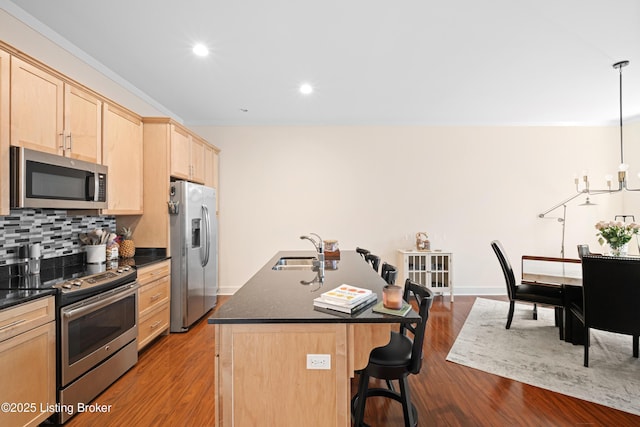 kitchen featuring decorative light fixtures, a center island with sink, stainless steel appliances, dark countertops, and a kitchen breakfast bar