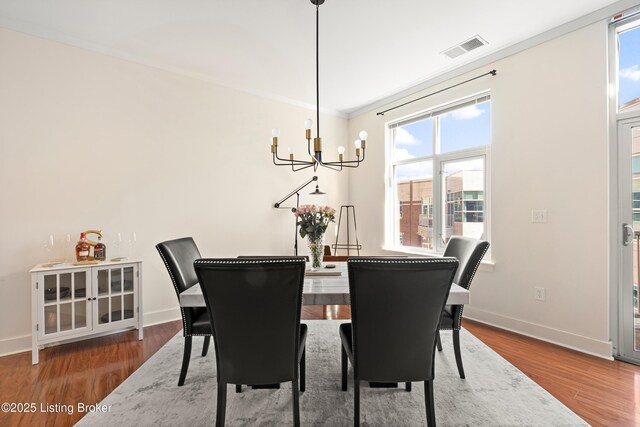 dining room with a notable chandelier, wood finished floors, visible vents, baseboards, and ornamental molding