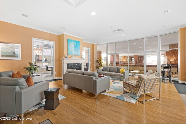 living area with crown molding, visible vents, light wood-style floors, a high end fireplace, and baseboards