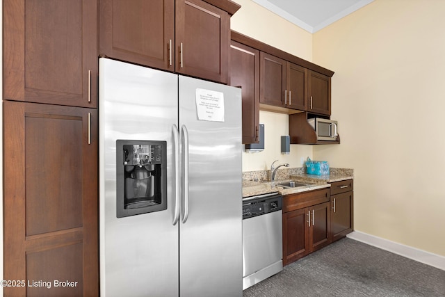 kitchen with baseboards, appliances with stainless steel finishes, light stone counters, crown molding, and a sink