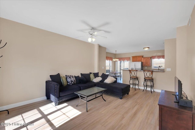 living room featuring ceiling fan with notable chandelier, light wood finished floors, and baseboards