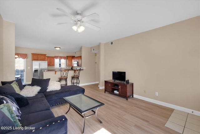 living area featuring light wood-type flooring, plenty of natural light, baseboards, and ceiling fan