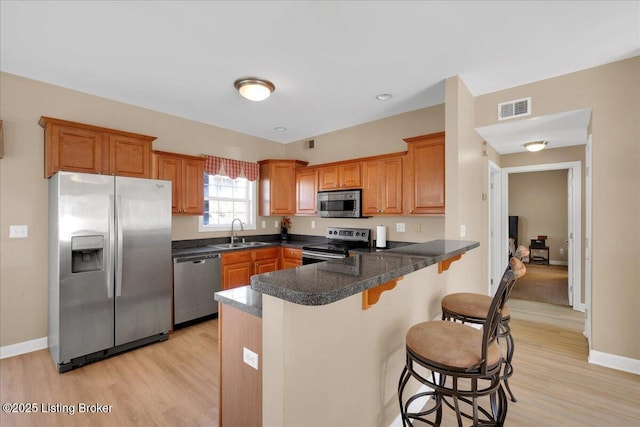 kitchen with visible vents, a peninsula, stainless steel appliances, a kitchen bar, and a sink