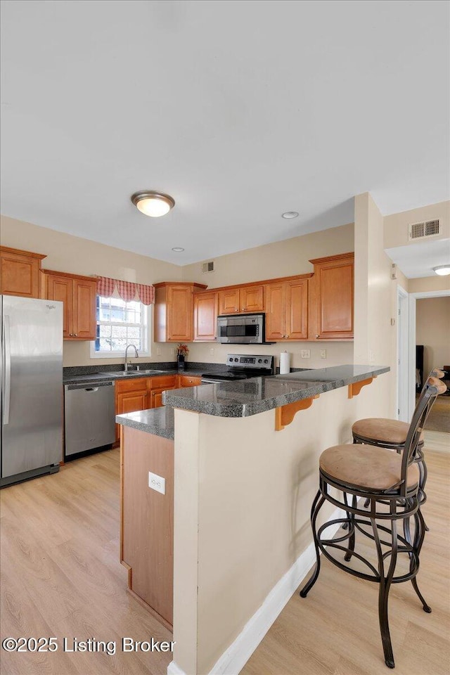 kitchen featuring light wood-style flooring, stainless steel appliances, a sink, visible vents, and a kitchen bar