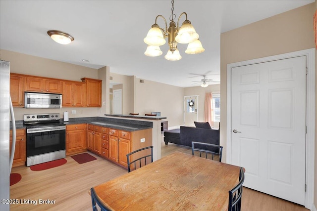 kitchen featuring brown cabinets, dark countertops, appliances with stainless steel finishes, light wood-type flooring, and a peninsula