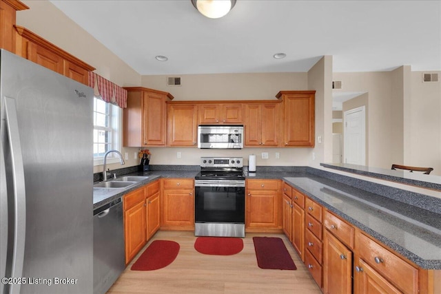 kitchen featuring visible vents, brown cabinetry, stainless steel appliances, light wood-type flooring, and a sink