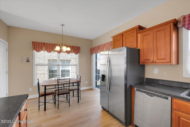 kitchen featuring light wood finished floors, dark countertops, appliances with stainless steel finishes, brown cabinets, and a chandelier