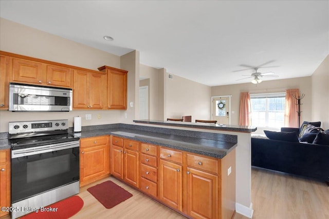 kitchen featuring open floor plan, a peninsula, appliances with stainless steel finishes, and light wood-style floors