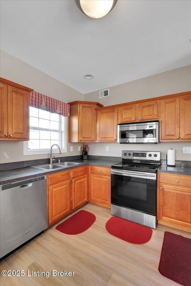 kitchen featuring light wood finished floors, visible vents, dark countertops, appliances with stainless steel finishes, and a sink