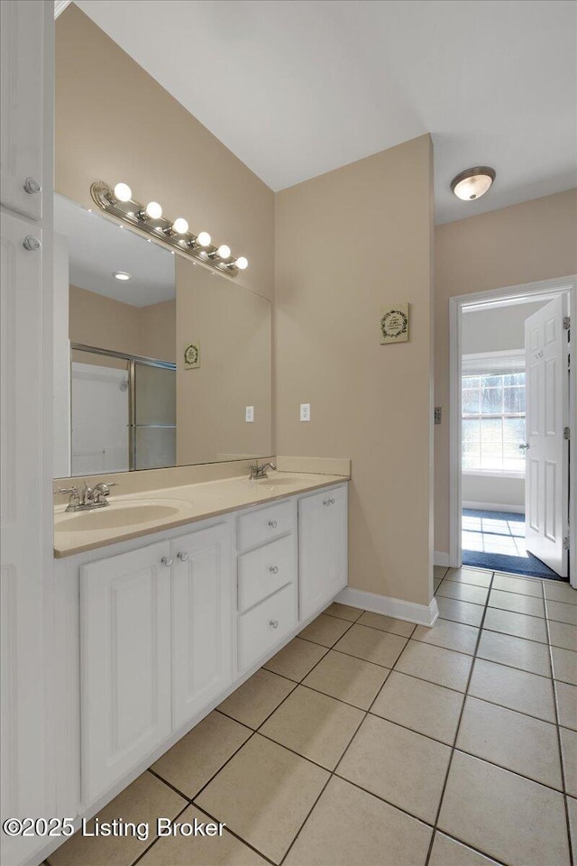 bathroom featuring a sink, baseboards, a shower stall, tile patterned floors, and double vanity