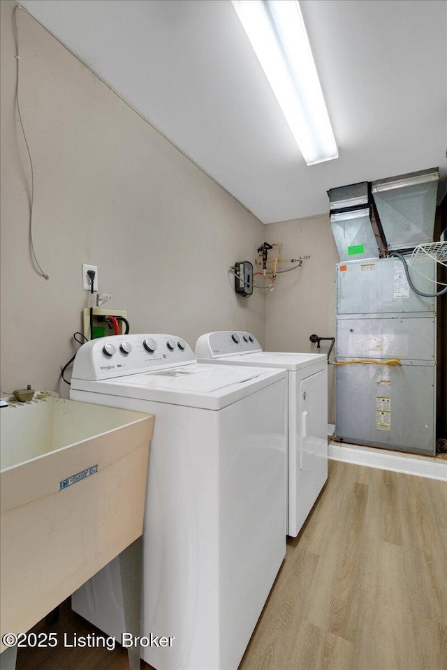 laundry room with washing machine and clothes dryer, heating unit, a sink, light wood-type flooring, and laundry area