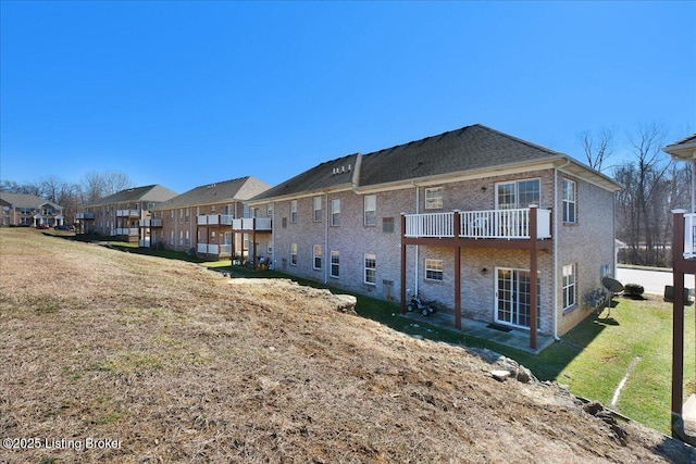 rear view of property featuring a residential view, brick siding, a lawn, and a balcony