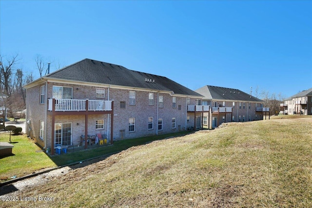 back of property with brick siding, a lawn, and a balcony