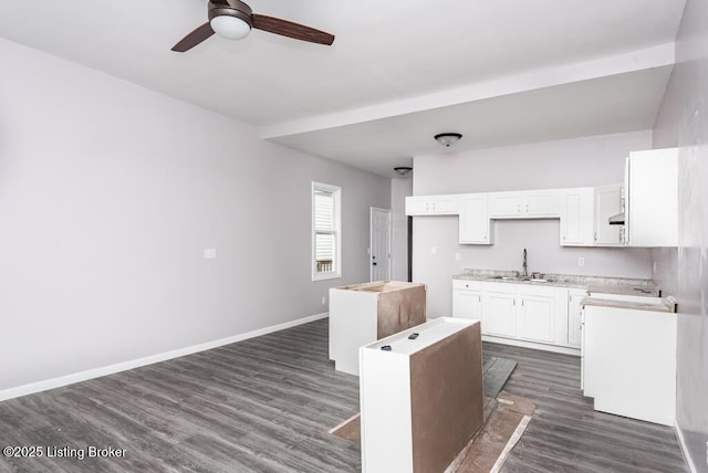 kitchen with dark wood-style flooring, light countertops, white cabinetry, a sink, and baseboards