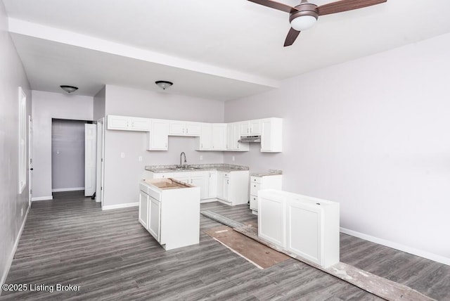 kitchen featuring a center island, light countertops, dark wood-type flooring, white cabinets, and a sink