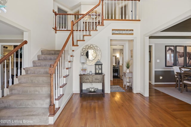 entryway with baseboards, a high ceiling, wood finished floors, and crown molding