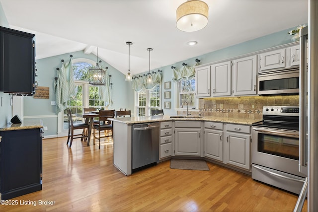 kitchen featuring a peninsula, appliances with stainless steel finishes, a sink, and light wood-style floors