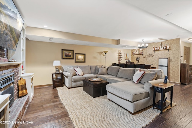 living area with baseboards, a glass covered fireplace, dark wood-style floors, an inviting chandelier, and recessed lighting